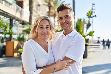 Middle age man and woman couple hugging each other standing at street