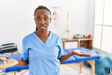 Black woman with braids working at pain recovery clinic clueless and confused with open arms, no idea concept.