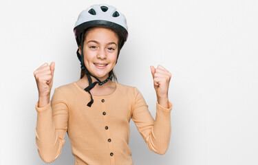 Beautiful brunette little girl wearing bike helmet screaming proud, celebrating victory and success very excited with raised arms