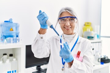 Middle age grey-haired woman wearing scientist uniform using pipette at laboratory
