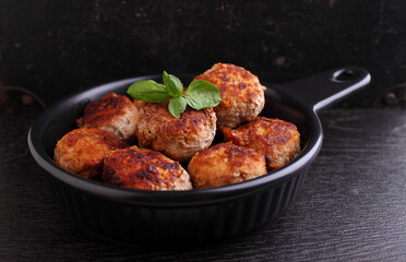 Meat cutlets decorated with basil in a black frying pan on a black background.