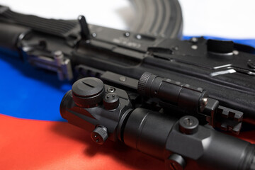 Closeup of a Russian made rifle with a red dot and magnifier optics on the Russian flag. 