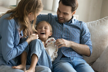 Happy sincere loving couple parents having fun tickling cute small child daughter, relaxing...