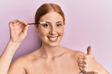Fototapeta premium Young irish woman holding eyelash curler smiling happy and positive, thumb up doing excellent and approval sign