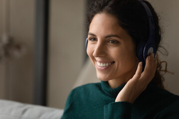 Digital headphones. Close up shot of smiling young latina woman wearing modern wireless earphones talking to customer online by video call. Skilled female interpreter translate virtual event remotely