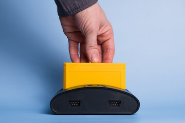 Man hand insert in old retro video game console cartridge. Isolated on blue.