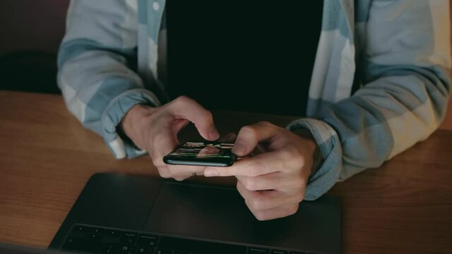 Hands of Man Freelancer Working at evening use smartphone and notebook. Close up. 4k. Male at workplace typing and Scroll phone.