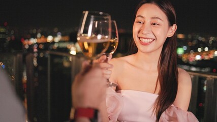 Young asian woman with sparklers is dancing and celebrating a new year. Fireworks, bengal lights in slow motion. Having fun at rooftop in the city.Happy interracial couple with glasses of wine .