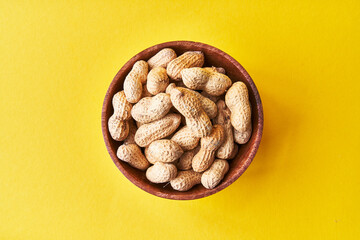  Bowl of peanuts with shell on a yellow background