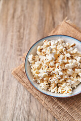  Bowl of salty popcorns on a wooden surface