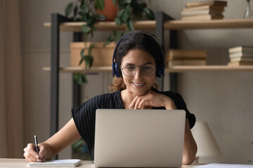 Busy latin female remote student listen to distant lecture course in headphones by laptop screen...