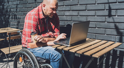 Freelancer with a physical disability in a wheelchair working at the street cafe