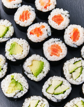  Group of avocado, salmon and cucumber sushi makis on a blackboard surface