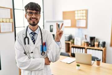 Hispanic man with beard wearing doctor uniform and stethoscope at the office smiling with happy...