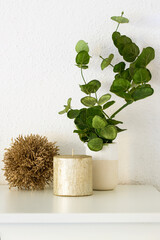 Festive still life composition. Gold candle, sparkle Christmas ball and eucalyptus branch on white table.