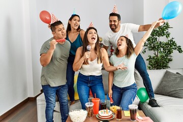 Group of young hispanic friends having birthday party singing song using microphone at home. - obrazy, fototapety, plakaty