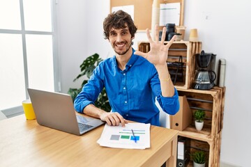 Young hispanic man with beard working at the office using computer laptop showing and pointing up...