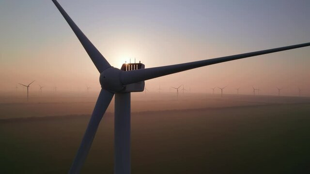 Close-up of wind turbine blades at sunset or sunrise. Windmills with rotating wings among green fields. Technology for wind energy, renewable energy source, earth care. Wind power station, drone video