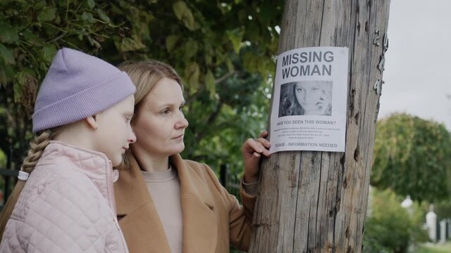 Sad mother with child stand at the ad about the missing young girl