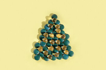 Supplements and vitamins in shape of christmas tree on yellow background, copy space.