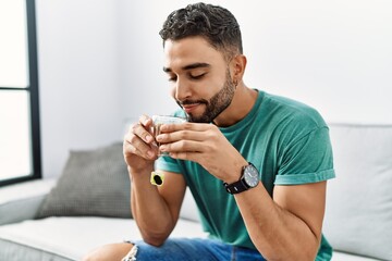 Young arab man drinking tea sitting on sofa at home