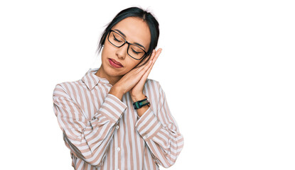 Young hispanic girl wearing casual clothes and glasses sleeping tired dreaming and posing with hands together while smiling with closed eyes.