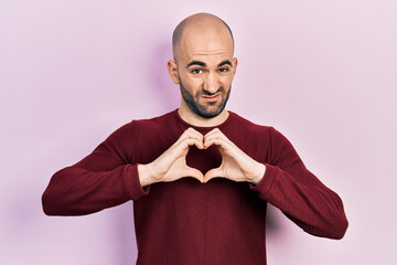 Young bald man doing heart symbol with hands clueless and confused expression. doubt concept.