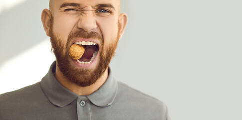 Confident, charismatic, handsome man winks his eye and cracks a hard nut. Close up head shot of a young ginger guy demonstrating his healthy teeth and trying to crack a walnut. Dental health concept - obrazy, fototapety, plakaty