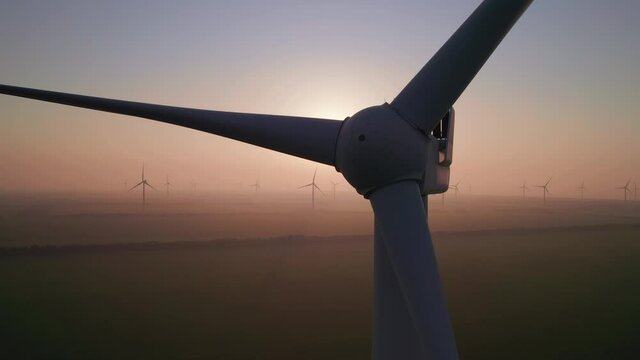 Close-up of wind turbine blades at sunset or sunrise. Windmills with rotating wings among green fields. Technology for wind energy, renewable energy source, earth care. Wind power station, drone video