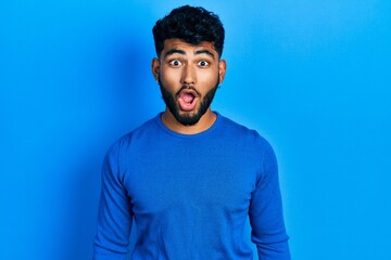 Fototapeta na wymiar Arab man with beard wearing casual blue sweater afraid and shocked with surprise expression, fear and excited face.