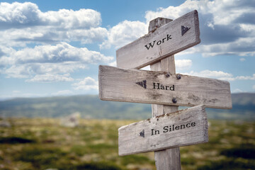 work hard in silence text quote on wooden signpost outdoors in nature. Blue sky above.