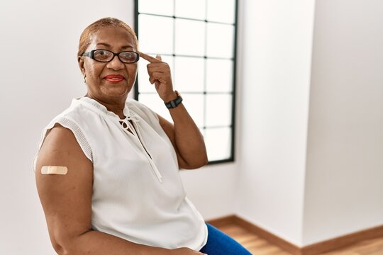 Mature Hispanic Woman Getting Vaccine Showing Arm With Band Aid Smiling Pointing To Head With One Finger, Great Idea Or Thought, Good Memory