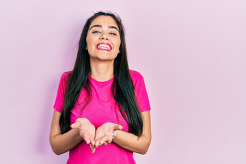 Fototapeta premium Young hispanic girl wearing casual pink t shirt smiling with hands palms together receiving or giving gesture. hold and protection
