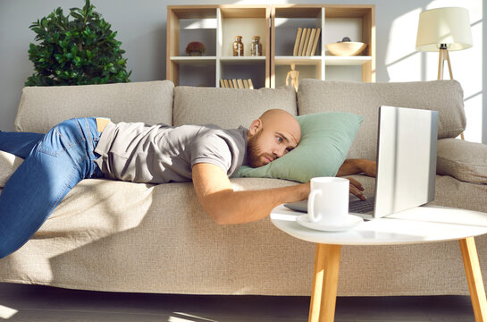 Man lying on sofa at home. Sad bored lazy passive guy resting alone on couch, looking at laptop computer screen, missing girlfriend in lockdown, waiting for job recruitment email, thinking about life