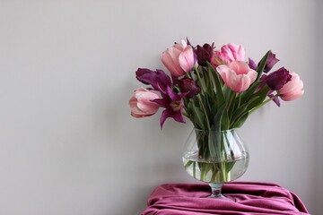 A huge bouquet made of pink and purple tulips in the glass vase on the white background