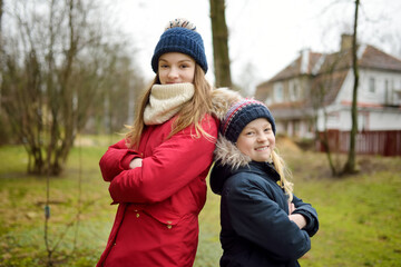 Two adorable young sisters having fun on beautiful winter day in a city. Cute children having a walk in winter town.