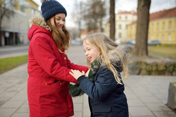 Two adorable young sisters having fun on beautiful winter day in a city. Cute children having a walk in winter town.