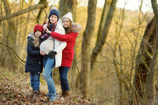 Young Pregnant Woman Hugging Her Older Daughters. Older Siblings Having Fun With Her Pregnant Mom Outdoors. Mother And Her Kids Spending Time Together.