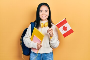 Young chinese girl exchange student holding canada flag smiling with a happy and cool smile on...