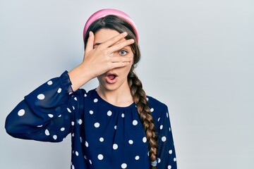 Young brunette girl wearing elegant look peeking in shock covering face and eyes with hand, looking through fingers with embarrassed expression.