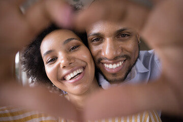 Happy young Black couple faces in finger heart shaped frame. Close up portrait. Millennial man and...