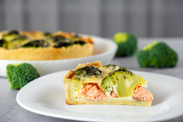 Classic Quiche with salmon, spinach and broccoli. Fish tart. Open faced salmon and broccoli quiche on kitchen table with broccoli pieces and savory pie on background.