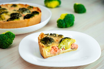 Open faced salmon and broccoli quiche on kitchen table with broccoli pieces and savory pie on background. Recipe of homemade fish pie of Mediterranean cuisine. Healthy eating or low card diet.