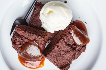 Vegan brownie squares with a scoop of dairy-free ice cream and apple caramel in white plate.