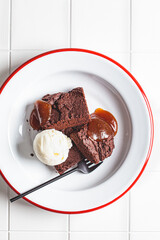 Vegan brownie squares with a scoop of dairy-free ice cream and apple caramel in white plate.