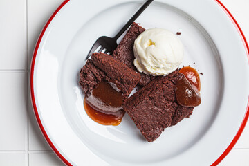 Vegan brownie squares with a scoop of dairy-free ice cream and apple caramel in white plate.