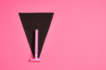 pink plastic disposable razor and black paper triangle on pink background