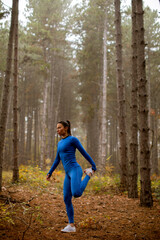 Young woman in blue track suit stretching before workout in the autumn forest