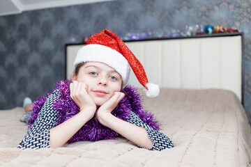 Charming girl lies on a large bed with a Santa Claus cap on her head