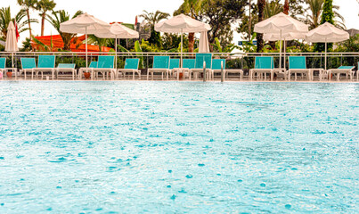 Swimming pool in the rain on a background of sunbeds and umbrellas